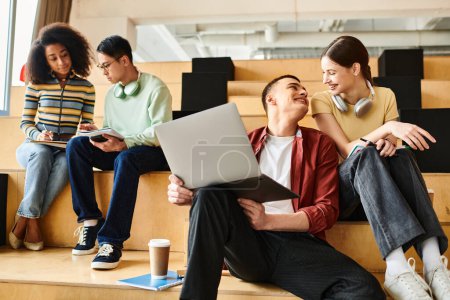 Groupe multiculturel de jeunes adultes assis sur un banc, absorbés par les ordinateurs portables, collaborant à des missions éducatives.