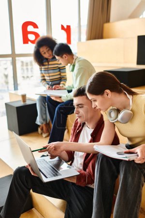 Multikulturelle Studentengruppe auf Bank sitzend, in Laptops vertieft, arbeitet und arbeitet in Innenräumen.