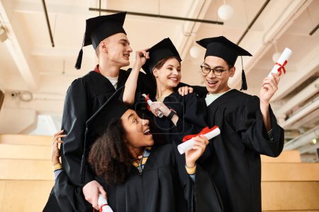 Un grupo diverso de estudiantes felices con batas de graduación y gorras académicas posando para una foto en el interior.