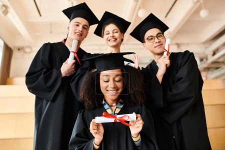 Diverse glückliche Studenten posieren in Abschlusskleidern und -mützen für ein festliches Bild drinnen.