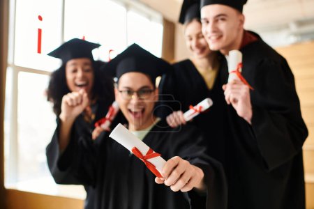 A diverse group of happy students in graduation gowns holding diplomas.