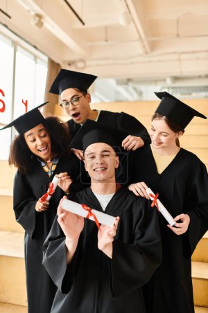 Un grupo diverso de estudiantes en trajes de graduación y gorras académicas posando felizmente para una foto en el interior.