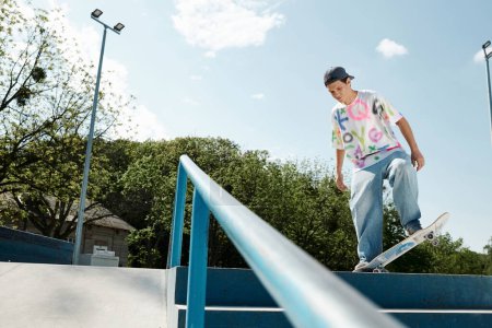 Téléchargez les photos : Un jeune patineur monte sans peur sa planche à roulettes sur le côté d'un rail dans un skate park extérieur coloré par une journée d'été ensoleillée. - en image libre de droit