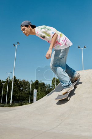 Téléchargez les photos : Un jeune homme glisse sans effort sur le côté d'une rampe sur sa planche à roulettes dans un skate park extérieur animé par une journée d'été ensoleillée. - en image libre de droit