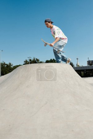 Photo for A young skater boy confidently rides his skateboard down the steep side of a ramp in an outdoor skate park on a sunny summer day. - Royalty Free Image