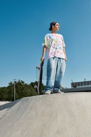 A young skater boy confidently stands on top of a skateboard ramp, ready to perform daring tricks in a summer skate park.
