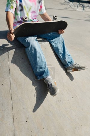 Un hombre se sienta en el suelo, sosteniendo un monopatín, profundamente en el pensamiento.