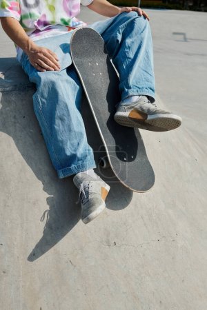 A young skater boy sits confidently on a skateboard, ready to glide on a ramp in an outdoor skate park on a sunny summer day.