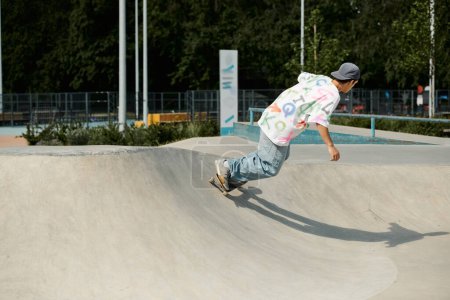 Téléchargez les photos : Un jeune patineur monte en toute confiance sa planche à roulettes sur le côté d'une rampe dans un skate park ensoleillé d'été. - en image libre de droit