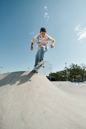 Téléchargez les photos : Jeune patineur garçon monte skateboard côté bas de la rampe extérieure dans le skate park d'été. - en image libre de droit