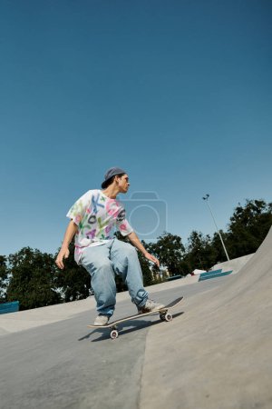Foto de Un joven skater monta su monopatín sin miedo por el lado de una rampa en un animado parque de skate al aire libre en un día de verano.. - Imagen libre de derechos