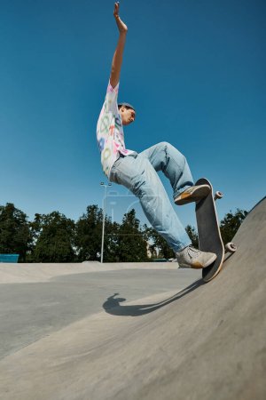 Foto de Un joven skater monta sin miedo su monopatín por el lado empinado de una rampa en un soleado parque de skate al aire libre. - Imagen libre de derechos