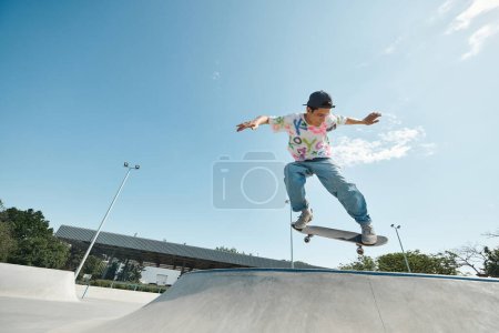 Téléchargez les photos : Un jeune patineur monte en toute confiance sa planche à roulettes sur le côté d'une rampe dans un skate park extérieur par une journée d'été ensoleillée. - en image libre de droit