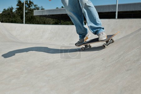 Téléchargez les photos : Jeune patineur garçon monte en toute confiance sa planche à roulettes sur la rampe à un skate park en plein air par une journée d'été ensoleillée. - en image libre de droit