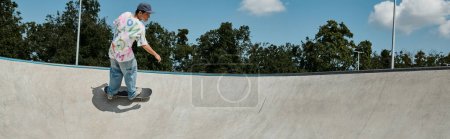 A young skater boy rides a skateboard up the ramp in an outdoor skate park on a sunny summer day.