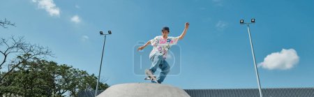A young skater boy daringly rides his skateboard on top of a cement ramp at a skate park outdoors on a summer day.