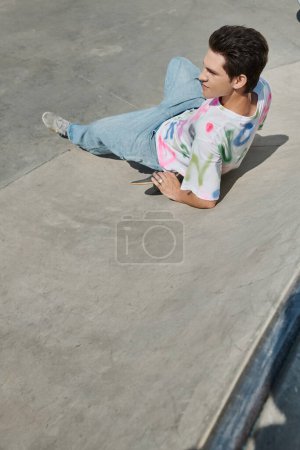 A man in casual attire lounging on the ground next to his skateboard, enjoying a moment of relaxation in a vibrant urban setting.