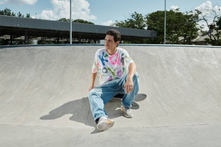 A young skater boy sits calmly on a skateboard in a bustling skate park on a sunny summer day.