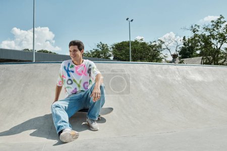 A young skater boy sits on his skateboard at a vibrant skate park on a sunny day, ready to kick and push into action.