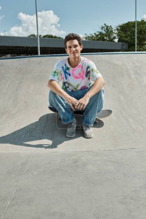 A young skater boy sitting confidently on his skateboard at a vibrant outdoor skate park on a sunny summer day.