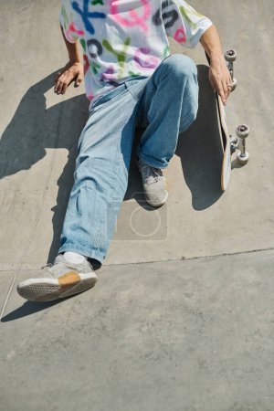 Ein junger Skater-Junge sitzt an einem sonnigen Sommertag auf seinem Skateboard in einem belebten Skatepark und überlegt seinen nächsten aufregenden Schachzug.