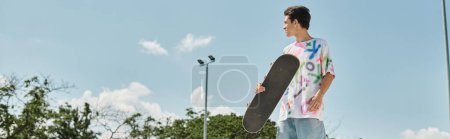 Photo for A young man holds a skateboard in his hand at a skate park outdoors on a summer day. - Royalty Free Image