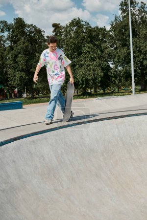 A young skater boy walking with skateboard up a steep ramp in a skate park on a sunny summer day.