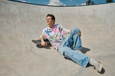 Un joven skater encuentra la paz sentado en un monopatín en un bullicioso parque de skate en un día soleado de verano.