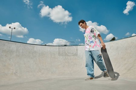 A young man, full of energy, holds his skateboard in a vibrant skate park on a sunny summer day.