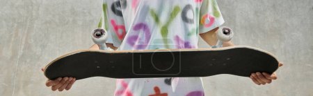 Téléchargez les photos : Un jeune patineur tenant une planche à roulettes à l'extérieur dans un skate park ensoleillé, se préparant pour une promenade passionnante lors d'une journée d'été. - en image libre de droit