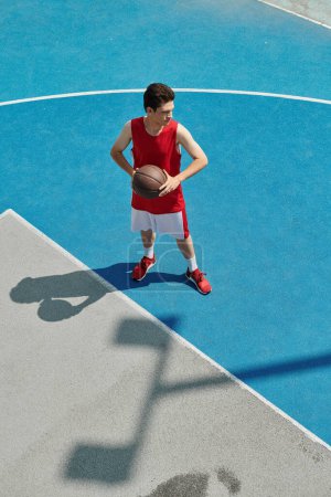 Un jeune homme talentueux tient avec confiance un ballon de basket tout en se tenant sur un terrain, perfectionnant ses compétences