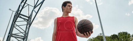 A young basketball player confidently dribbles a basketball while standing outdoors on a summer day
