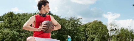 A young man donning a vibrant red shirt engages in a game of basketball outdoors on a sunny summer day.