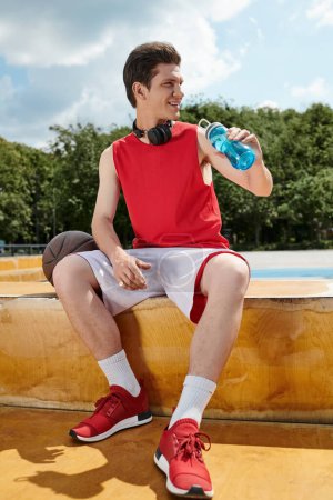 Un hombre sentado en una repisa, tomando un descanso para hidratarse con una botella de agua en la mano.