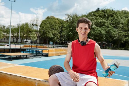 Foto de Un hombre con una camisa roja se sienta casualmente cerca del baloncesto disfrutando de un momento tranquilo. - Imagen libre de derechos