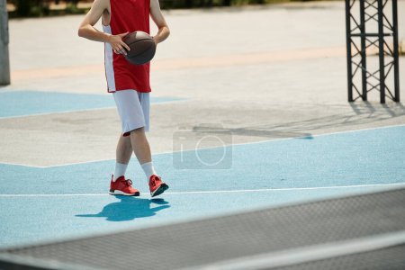 Un jeune homme se tient sur un terrain de basket tenant une balle, prêt à jouer sous le soleil d'été.