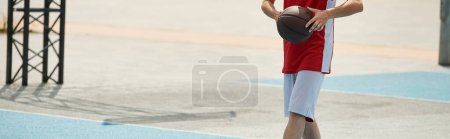 A young basketball player stands on top of a basketball court, confidently holding a ball on a sunny summer day.