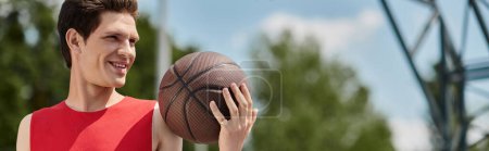 A young man in a red shirt skillfully dribbling a basketball outdoors on a warm summer day.