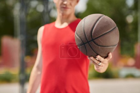 A young man in a vibrant red shirt showcases his basketball skills outdoors on a sunny day.