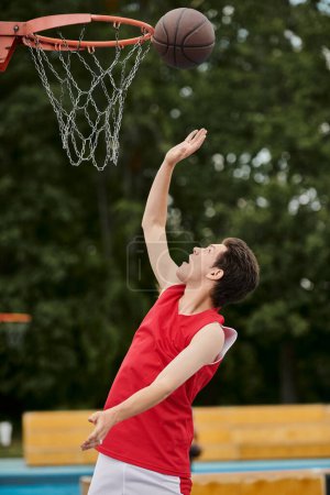 Ein junger Mann in leuchtend rotem Hemd dribbelt an einem sonnigen Sommertag gekonnt einen Basketball auf einem Außenplatz.