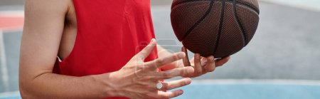 Młody koszykarz trzymający piłkę w dłoni, gotowy do gry na świeżym powietrzu w letni dzień.