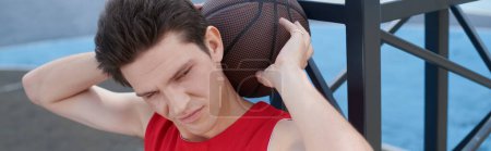 Téléchargez les photos : Jeune joueur de basket tient le basket-ball à la tête, profitant de la journée d'été en plein air. - en image libre de droit