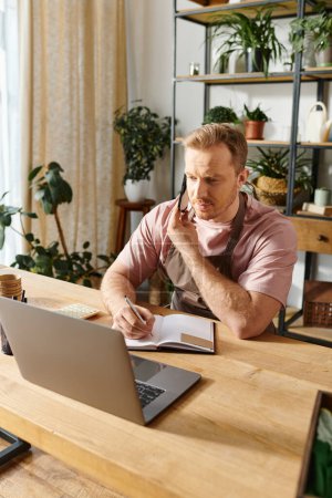 Foto de Un hombre con un ordenador portátil profundamente centrado en el funcionamiento de su pequeño negocio de la tienda de plantas con dedicación y espíritu empresarial. - Imagen libre de derechos