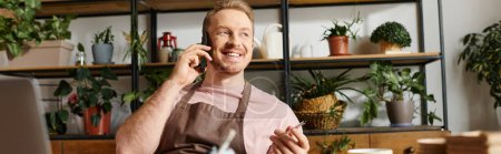 Ein fokussierter Mann sitzt an einem Schreibtisch in einem Pflanzengeschäft und führt ein Telefonat, während er sein kleines Geschäft führt.