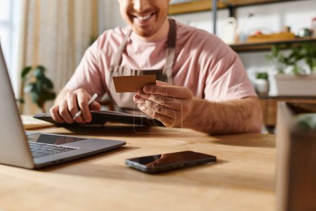 Un homme assis à une table avec un ordinateur portable et une carte de crédit, effectuant un achat en ligne pour sa petite entreprise.