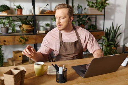 Ein Mann konzentriert sich auf seinen Laptop, vertieft in seine kleinen Geschäfte in einem Pflanzengeschäft.