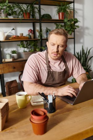 Un hombre se sienta en una mesa en una tienda de plantas, enfocado en su computadora portátil, encarnando al dueño de un exitoso negocio floral.