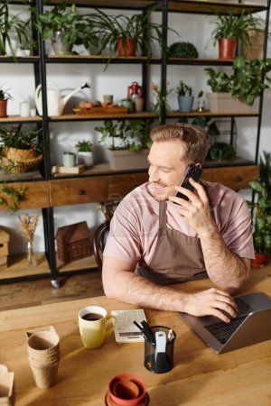Un hombre sentado en una mesa hablando por celular en una tienda de plantas, encarnando el concepto de ser dueño de una pequeña empresa.