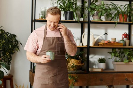 Téléchargez les photos : Un homme charmant, propriétaire d'un magasin de plantes, debout dans son tablier et tenant pot de plantes - en image libre de droit