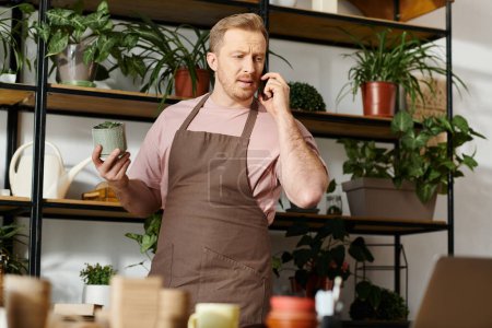 A man in an apron multitasks, taking a call while managing his plant shop business.